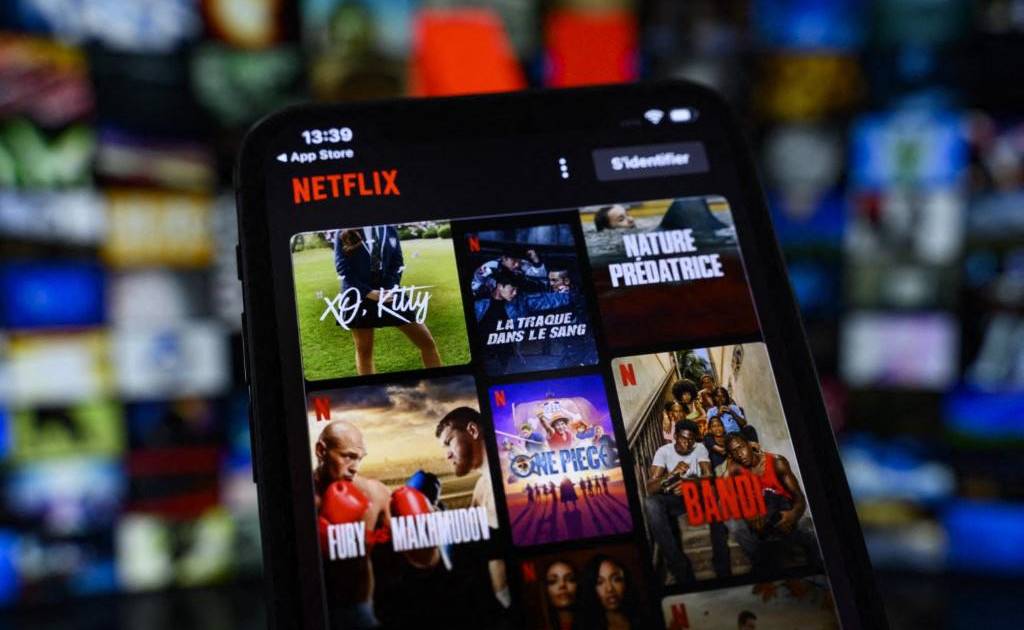 Una mano sosteniendo un control remoto apuntando a una pantalla de TV con la interfaz de Netflix