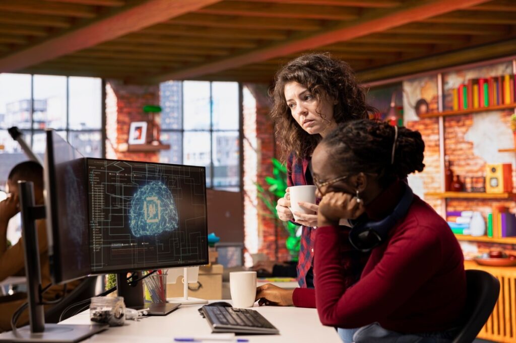 Una imagen de una persona frente a una pantalla de computadora con una expresión de preocupación, mientras una mano robótica se acerca a su teclado.