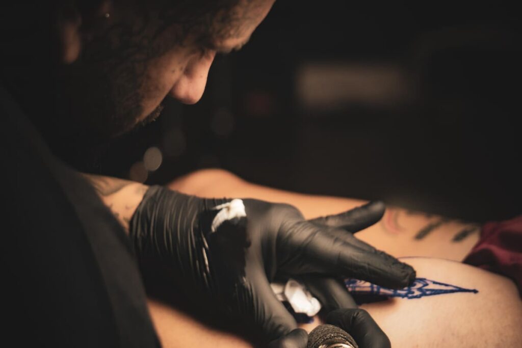 Un tatuador trabajando en un diseño en la piel de una persona, con una sonrisa de satisfacción