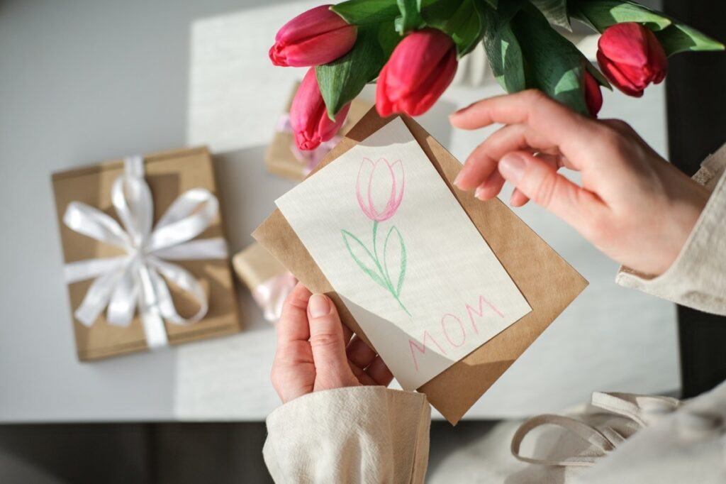 Madre sonriendo con regalos hechos a mano y una tarjeta de 'Feliz Día de las Madres'