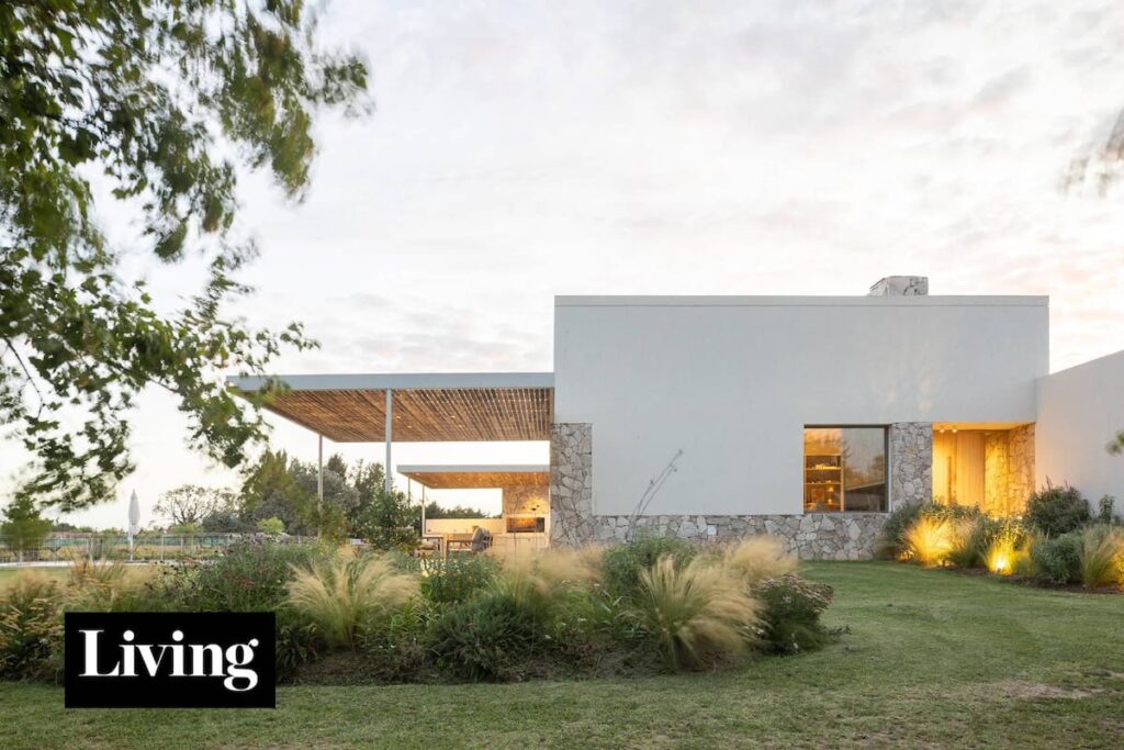 Una casa blanca con tres pérgolas 'voladoras' y un jardín con piedras y madera en Luján