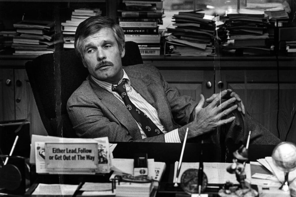 Imagen de Ted Turner en su despacho de CNN, con una sonrisa de determinación mientras mira hacia el futuro de la televisión.