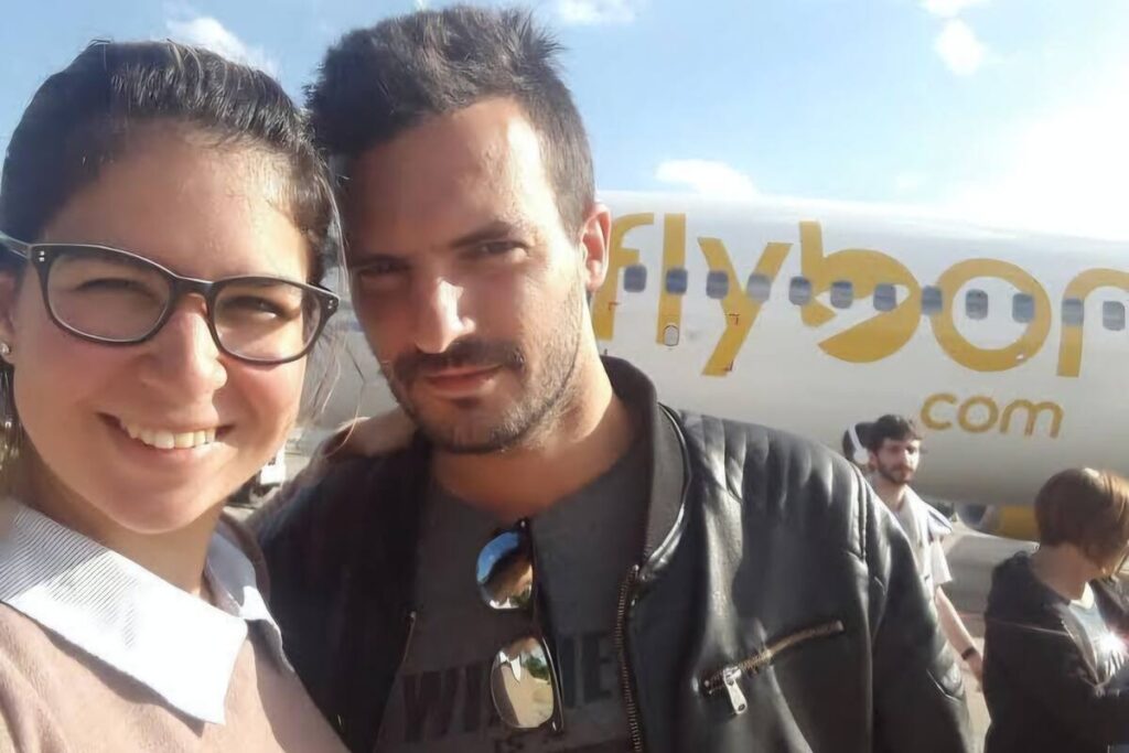 Una pareja sonriendo juntos, con un entorno de oficina o lugar de trabajo, con una moto en el fondo
