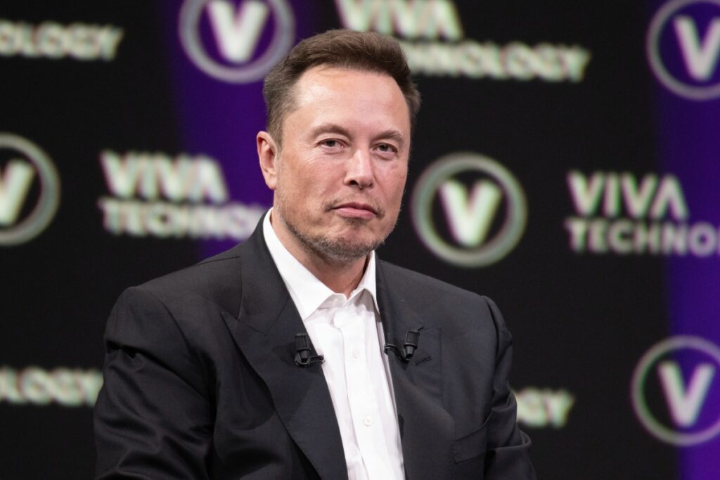 Elon Musk sonriendo mientras mira una pantalla con gráficos financieros que reflejan el crecimiento de su patrimonio