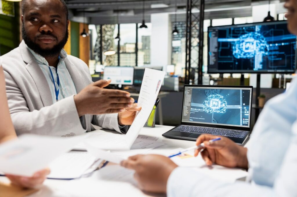 Una imagen de una persona trabajando en una oficina con una tableta, con un engranaje de IA en el fondo