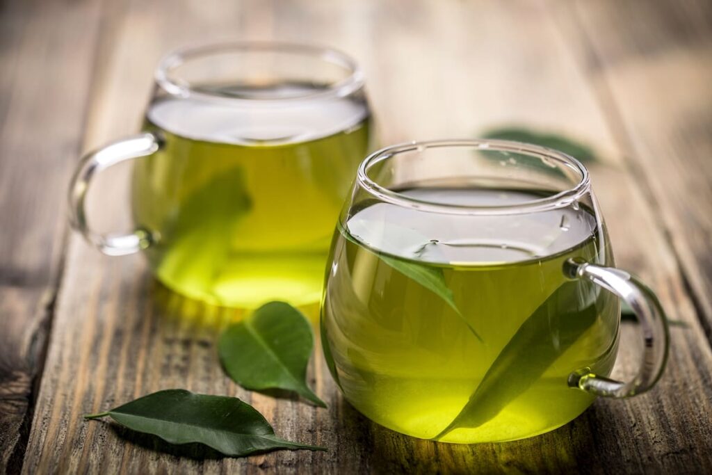 Una taza de té verde caliente con hojas de té verde fresco