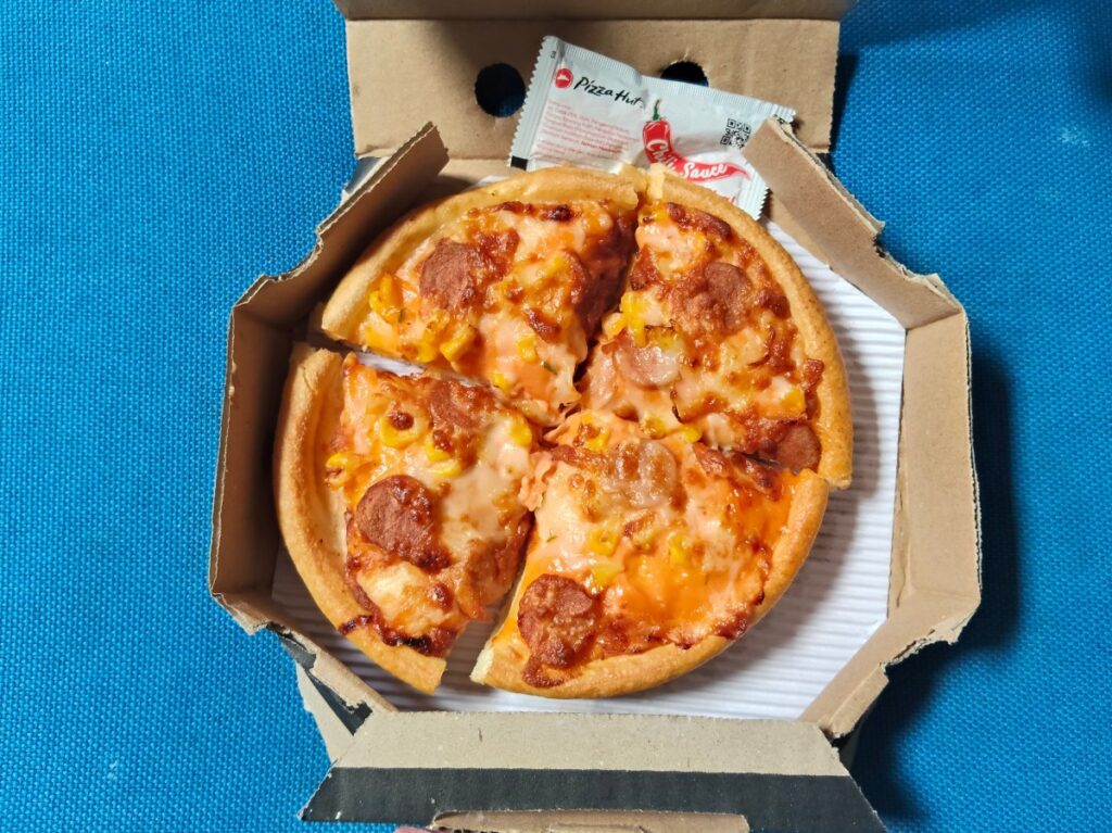 Persona sosteniendo una pizza personal de Pizza Hut con un distintivo BOOK IT! al fondo