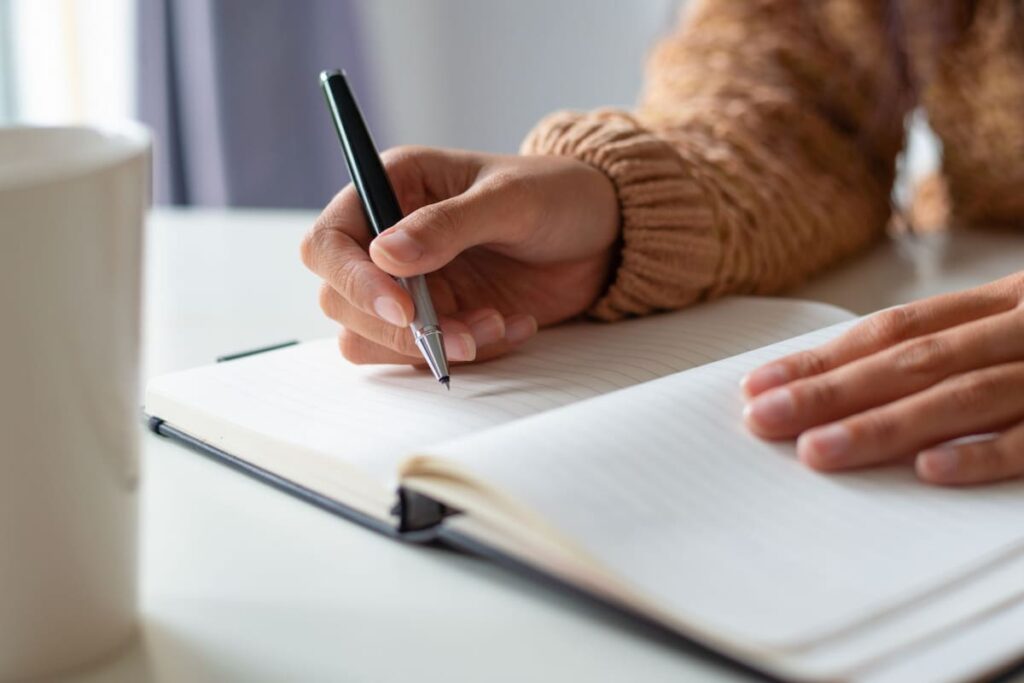 Persona escribiendo a mano en un cuaderno con un lápiz