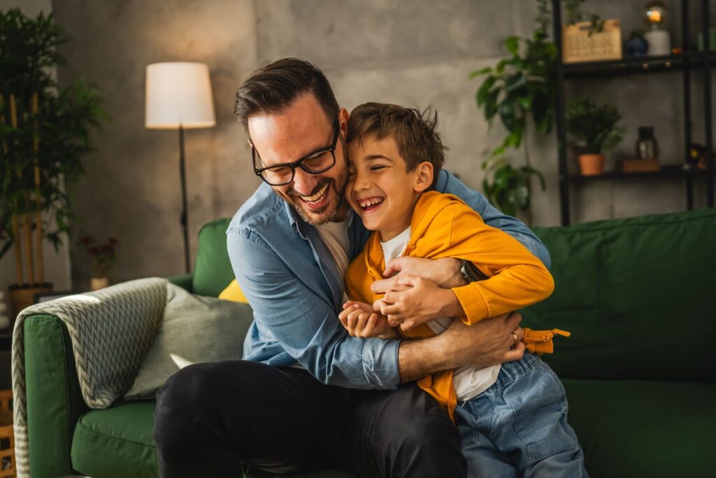 Un padre sonriendo mientras abre un regalo de ropa y relojes para el Día del Padre