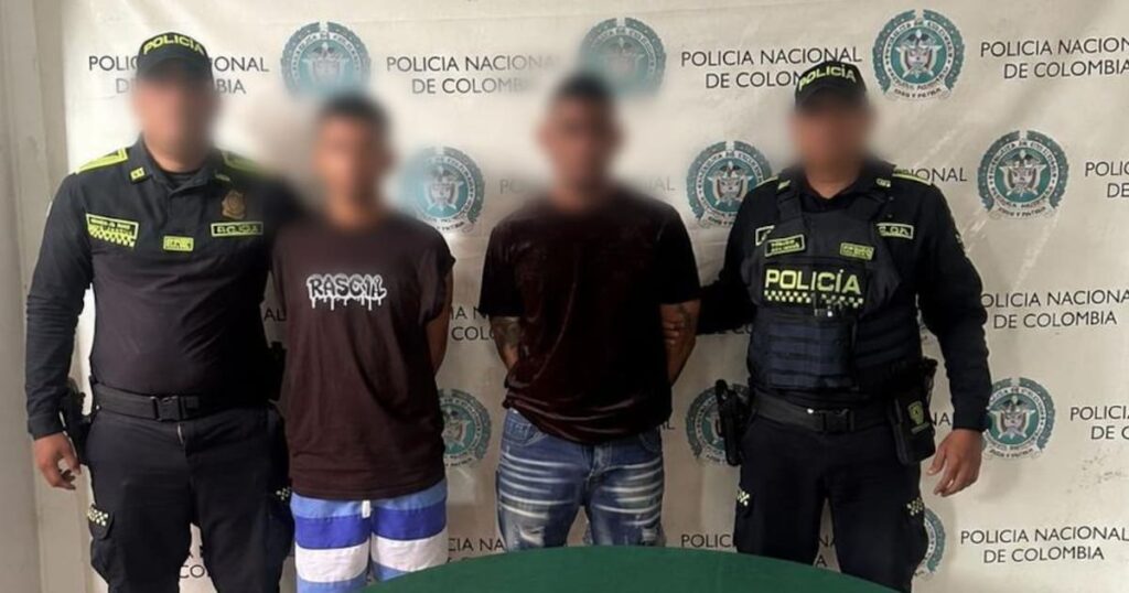 Dos hombres esposados por policías, con una granada y panfletos extorsivos incautados.